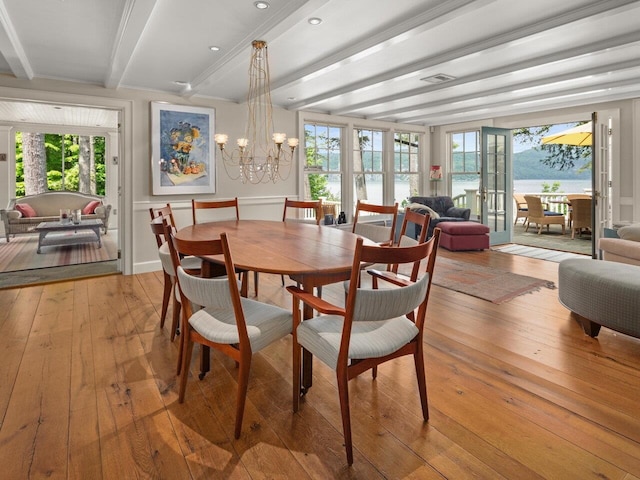 dining room featuring a healthy amount of sunlight, a notable chandelier, light wood-style flooring, and beamed ceiling