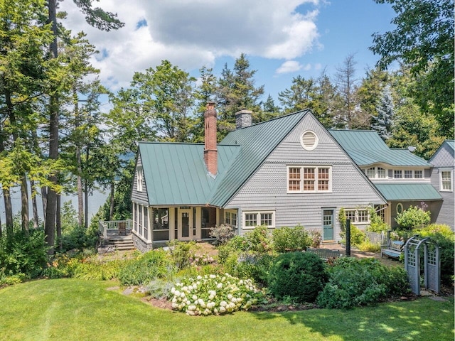 rear view of house with a chimney, a lawn, a sunroom, a standing seam roof, and metal roof