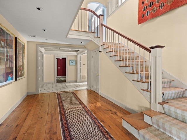 stairway featuring a high ceiling, visible vents, baseboards, and hardwood / wood-style flooring