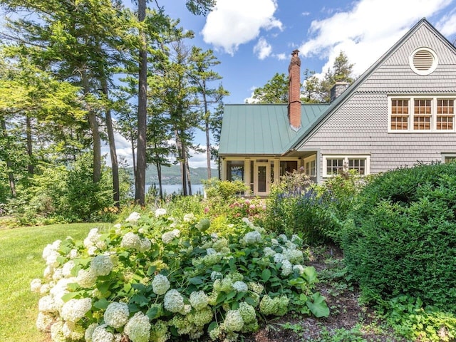 back of house with metal roof, a standing seam roof, and a chimney