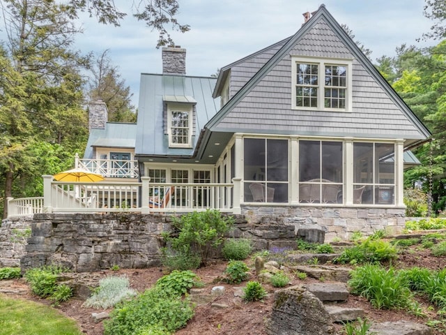 back of house with a sunroom, a chimney, metal roof, and a standing seam roof