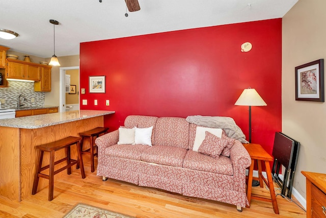 living area featuring light wood-style floors, baseboards, and a ceiling fan