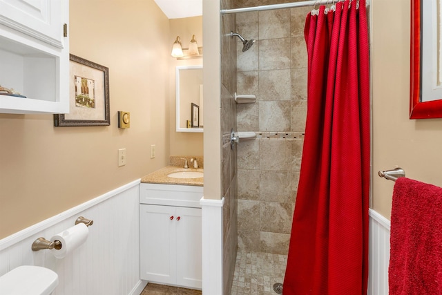 bathroom with toilet, vanity, tiled shower, and wainscoting