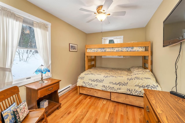 bedroom with ceiling fan, a baseboard radiator, wood finished floors, and baseboards