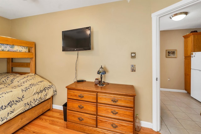 bedroom featuring light tile patterned floors, freestanding refrigerator, and baseboards