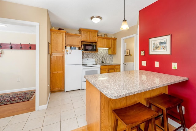 kitchen featuring light tile patterned floors, decorative backsplash, a sink, white appliances, and a kitchen breakfast bar