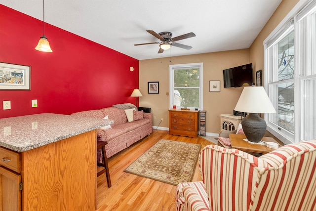 living room with ceiling fan, an accent wall, light wood-type flooring, and baseboards