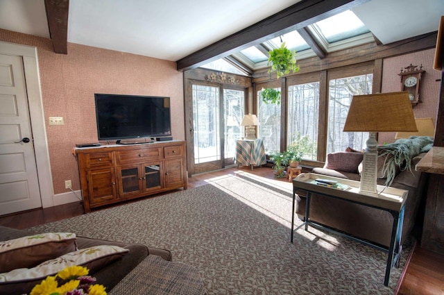 living room featuring wallpapered walls, vaulted ceiling with skylight, baseboards, and wood finished floors