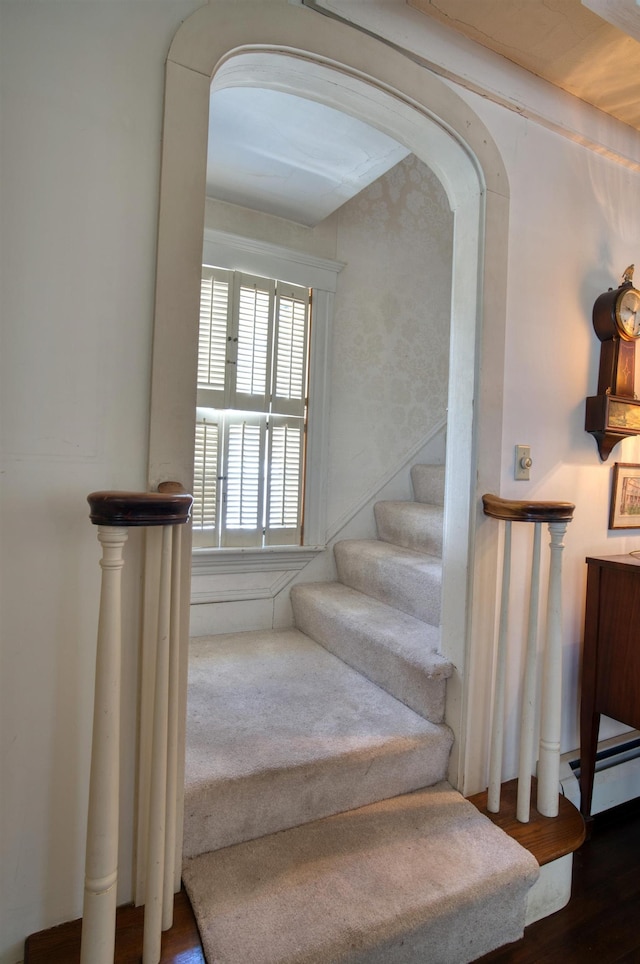 stairway with arched walkways, baseboard heating, and wood finished floors