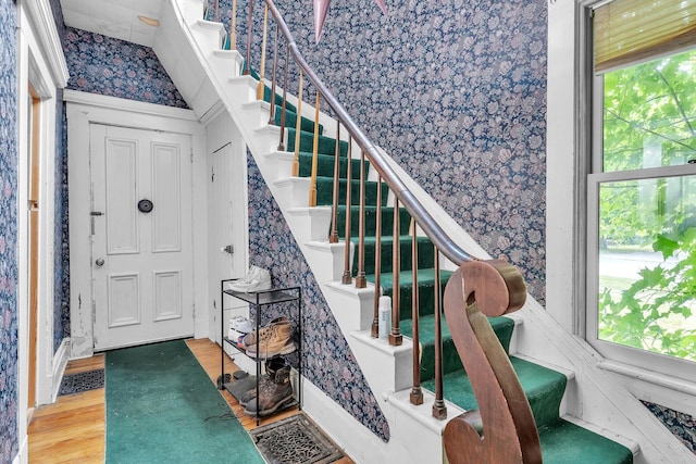 stairs with wallpapered walls and wood finished floors