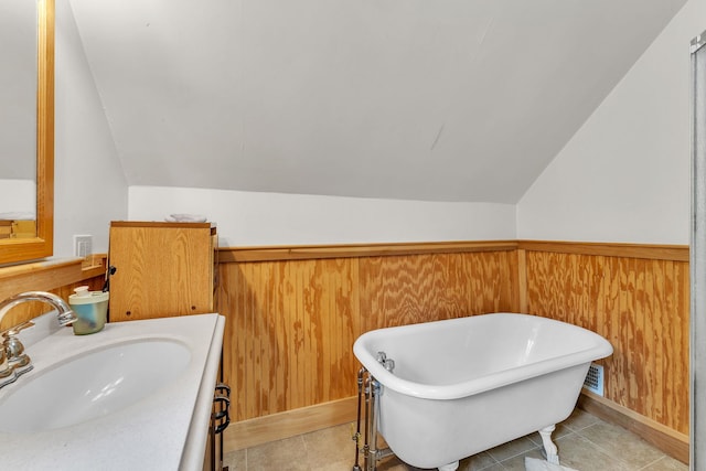 bathroom with lofted ceiling, a soaking tub, a wainscoted wall, and wood walls