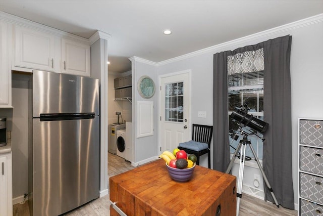 kitchen featuring white cabinets, light wood-type flooring, freestanding refrigerator, washing machine and clothes dryer, and crown molding