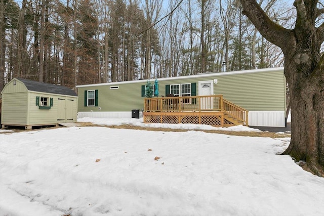 snow covered rear of property featuring an outbuilding, a deck, and a storage shed