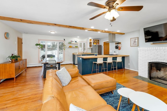 living room with a fireplace, light wood finished floors, a baseboard heating unit, ceiling fan, and baseboards