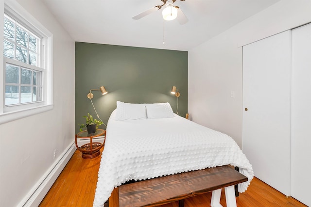 bedroom featuring baseboards, a baseboard radiator, ceiling fan, wood finished floors, and a closet