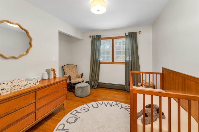 bedroom with a baseboard heating unit, a crib, and wood finished floors