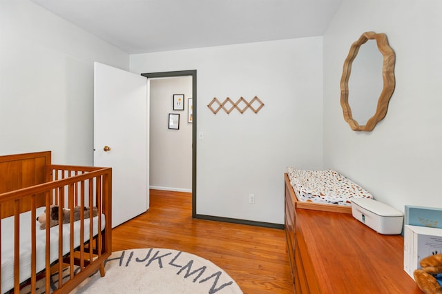 bedroom with a crib, wood finished floors, and baseboards