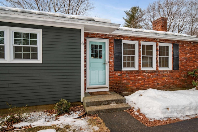 view of exterior entry with brick siding and a chimney