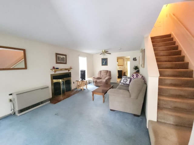 living room with a fireplace with raised hearth, a ceiling fan, heating unit, stairs, and carpet flooring