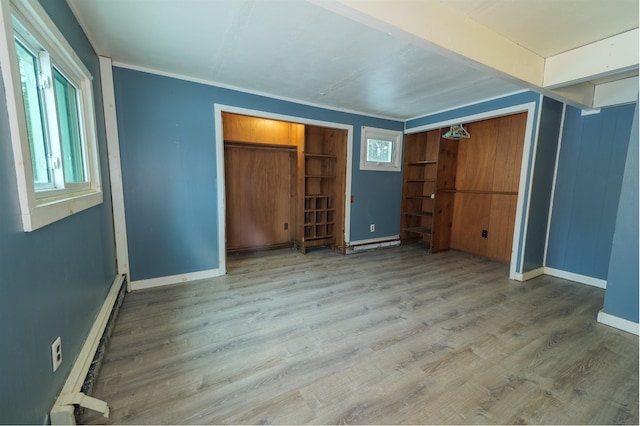 unfurnished bedroom featuring multiple windows, a baseboard radiator, wood finished floors, and baseboards