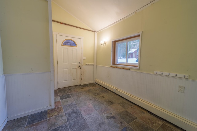 foyer entrance with a baseboard radiator, stone finish flooring, a wainscoted wall, and vaulted ceiling