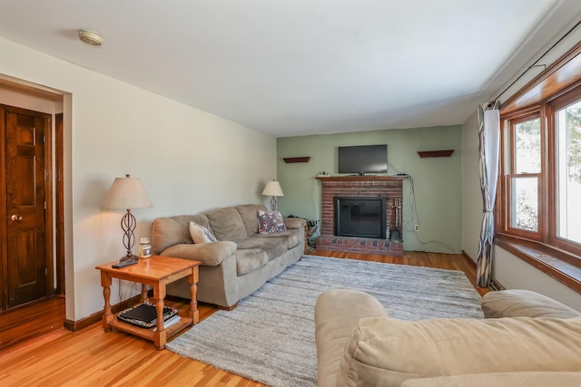 living room featuring a brick fireplace, baseboards, and wood finished floors