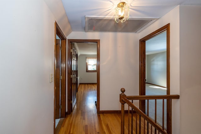 hallway with light wood-type flooring, baseboards, and an upstairs landing