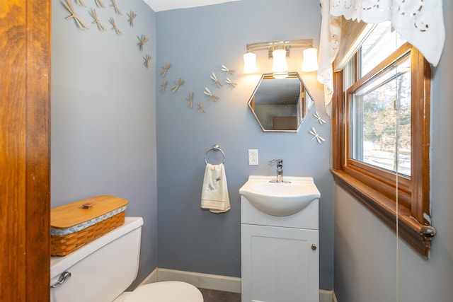 half bathroom with toilet, baseboards, and vanity