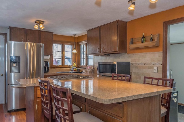 kitchen featuring appliances with stainless steel finishes, a sink, light countertops, a kitchen bar, and backsplash