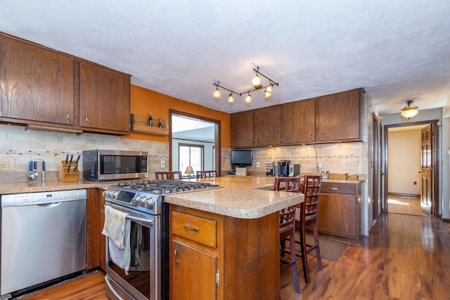 kitchen featuring a peninsula, appliances with stainless steel finishes, dark wood-style flooring, and light countertops