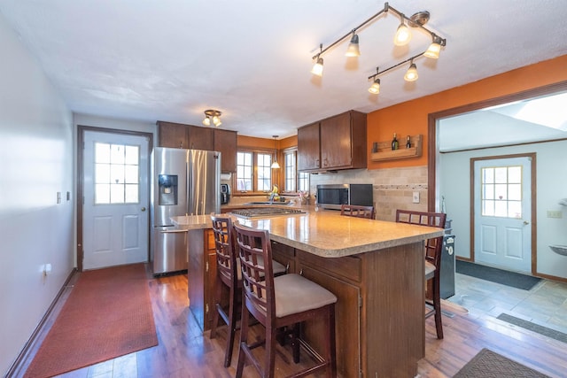 kitchen with dark wood finished floors, light countertops, backsplash, appliances with stainless steel finishes, and a kitchen breakfast bar