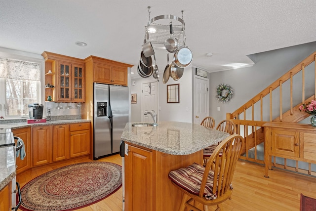 kitchen with light wood finished floors, appliances with stainless steel finishes, brown cabinetry, and a sink