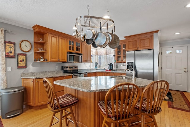 kitchen with brown cabinets, stainless steel appliances, crown molding, light wood-type flooring, and a sink