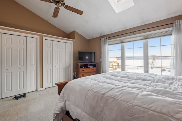 carpeted bedroom featuring lofted ceiling with skylight, ceiling fan, and two closets