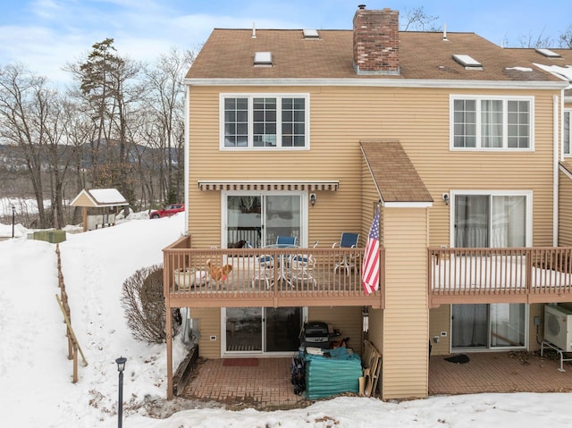 snow covered house featuring ac unit and a chimney