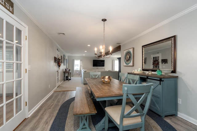 dining area featuring crown molding, a notable chandelier, visible vents, wood finished floors, and baseboards