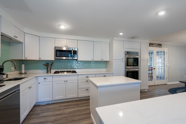 kitchen with stainless steel appliances, a sink, white cabinetry, light countertops, and backsplash