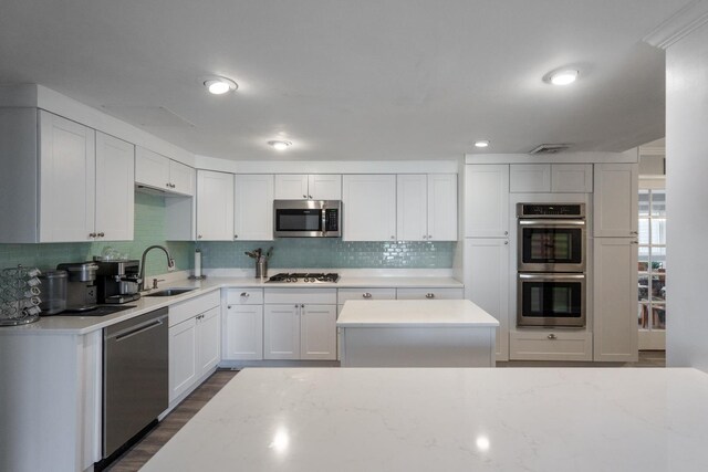 kitchen with backsplash, appliances with stainless steel finishes, dark wood-type flooring, white cabinets, and a sink