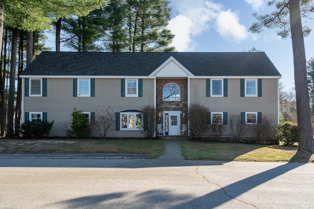 view of front facade featuring stone siding, a shingled roof, and a front yard