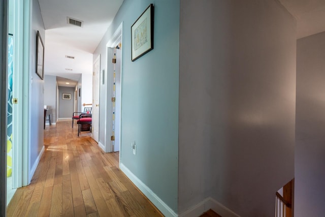 hall with baseboards, visible vents, and light wood finished floors