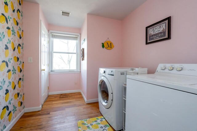 clothes washing area with washer and dryer, visible vents, light wood-type flooring, laundry area, and baseboards