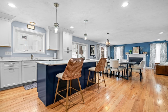 kitchen with light countertops, open floor plan, a kitchen island, a sink, and light wood-type flooring