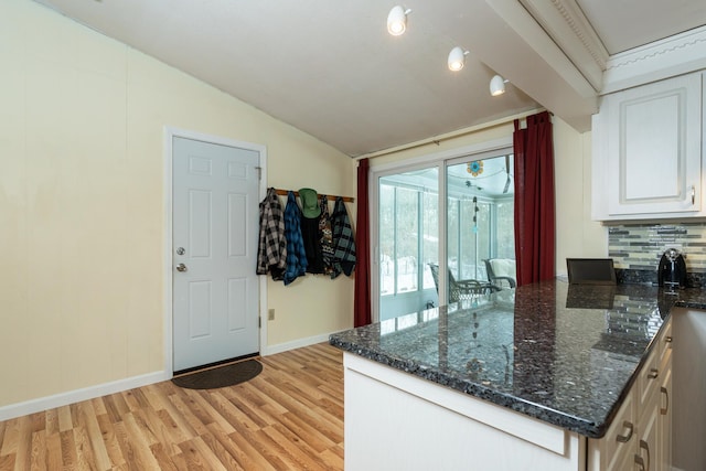 kitchen with dark stone countertops, vaulted ceiling, backsplash, and light wood finished floors