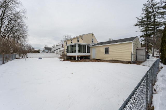 snow covered rear of property with a fenced backyard and a sunroom