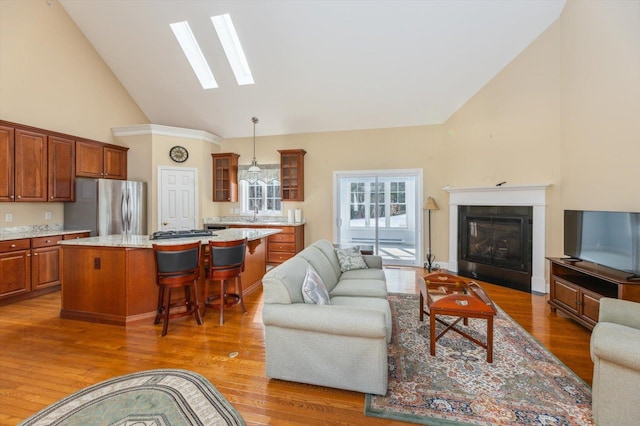 living room featuring a skylight, light wood-style flooring, high vaulted ceiling, and a glass covered fireplace