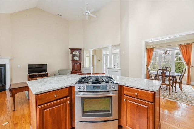 kitchen with a glass covered fireplace, gas range, light stone counters, open floor plan, and ornate columns