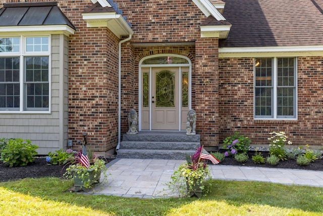 doorway to property featuring a shingled roof and brick siding