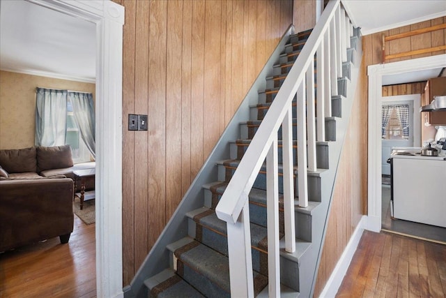 stairs with baseboards, wooden walls, ornamental molding, and hardwood / wood-style floors