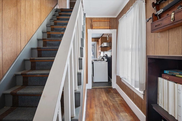 staircase featuring wood walls, wood-type flooring, washer / clothes dryer, and crown molding