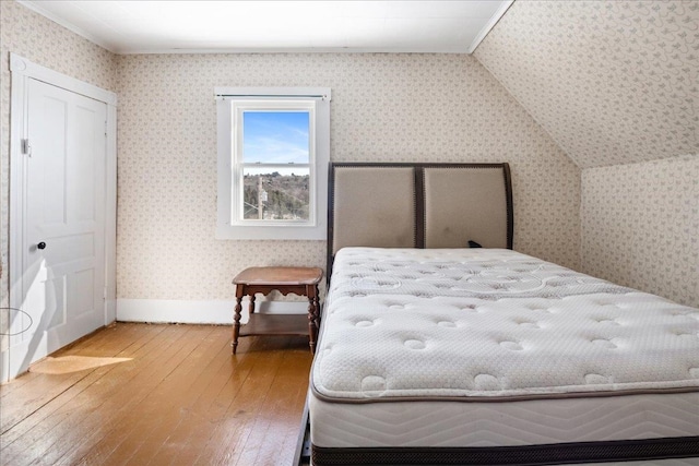 bedroom featuring lofted ceiling, wood-type flooring, baseboards, and wallpapered walls